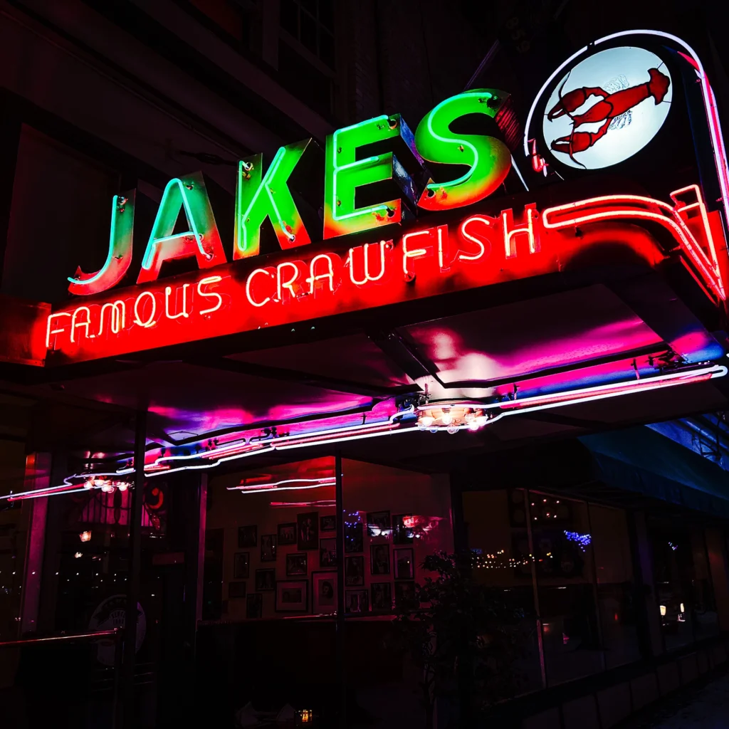 Jakes Famous Crawfish neon sign glowing green at night — Noir10 handmade LED backlit print